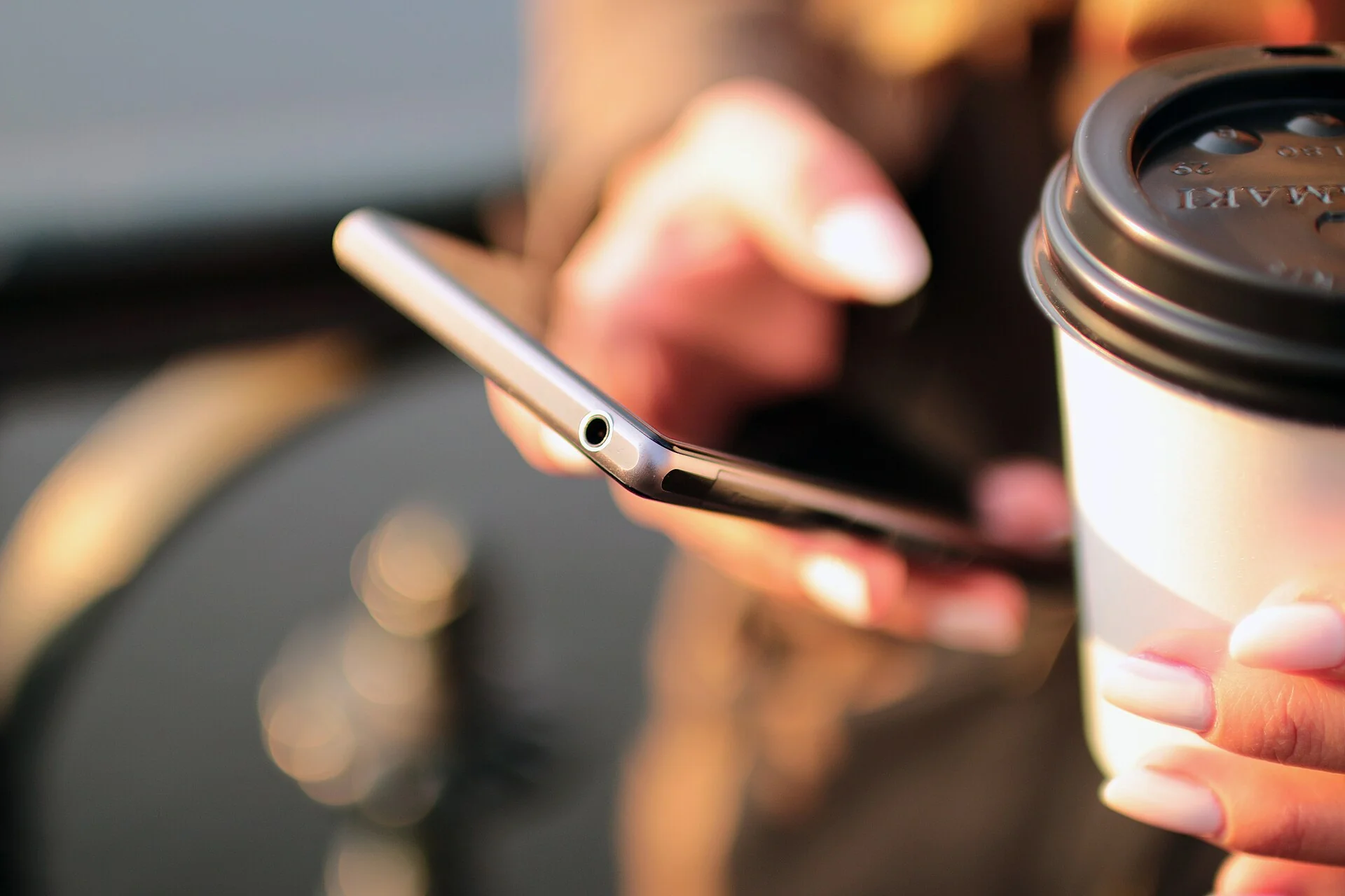 Manos sostienen un teléfono móvil junto a una taza de café.