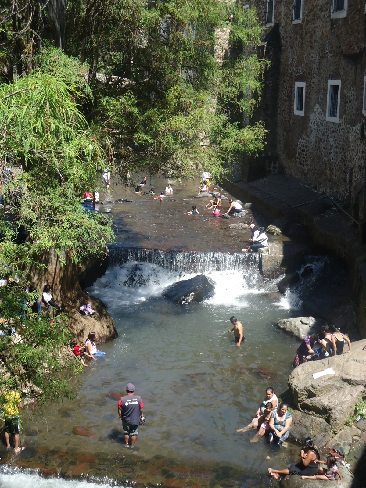 Tramo del río Chalma con vegetación, edificios y visitantes.